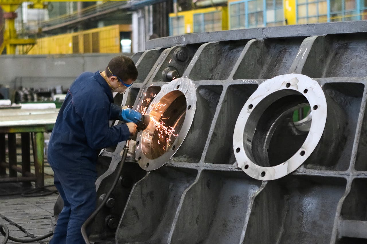 gallery-6 A worker in protective gear grinding metal, creating sparks in a factory setting.